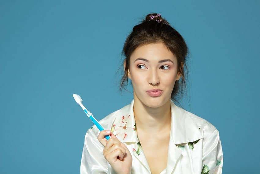 A woman smirks while just finishing brushing her teeth - one of the top things to do twice a day to prevent gum disease