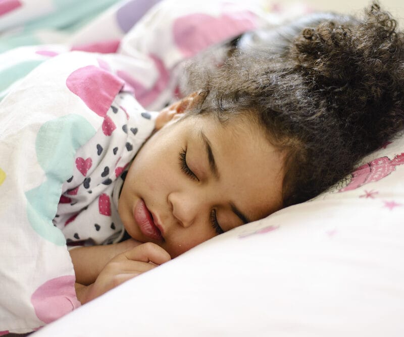 Young girl resting soundly under a blanket with a calm expression, representing improved sleep quality in children – Pediatric Sleep Apnea