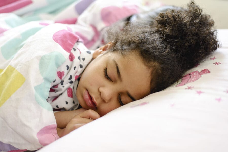 Young girl resting soundly under a blanket with a calm expression, representing improved sleep quality in children – Pediatric Sleep Apnea