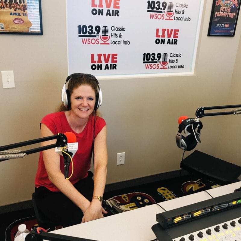 Smiling woman with headphones in a radio station studio, sitting between microphones during a live broadcast discussing TMJ disorders and sleep apnea