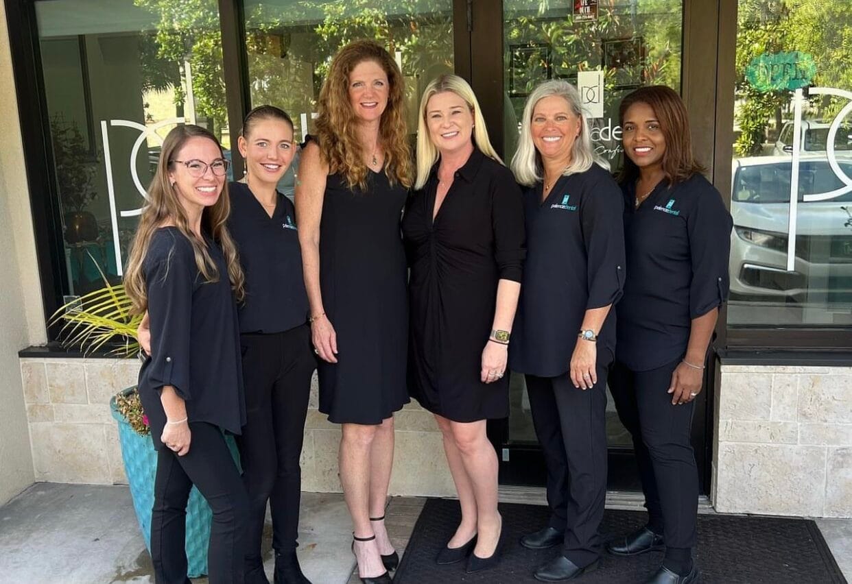 Dr. Stephanie Kinsey, standing with her five smiling staff members in black outfits, outside the Palencia Dental office – Palencia Dental