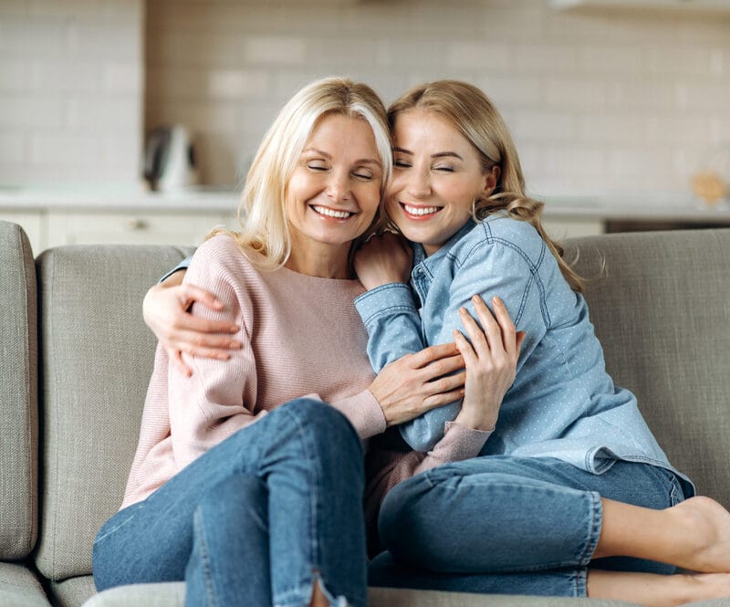 Happy mother and daughter hugging on a couch with radiant smiles, symbolizing the joy and health benefits of maintaining a cavity-free lifestyle