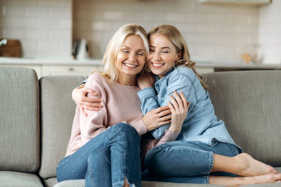 Happy mother and daughter hugging on a couch with radiant smiles, symbolizing the joy and health benefits of maintaining a cavity-free lifestyle