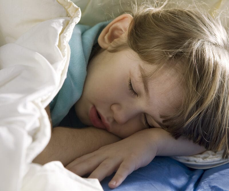 Young child asleep on a bed under blankets, representing topics related to nighttime routines and managing a child’s bed-wetting with comfort and care