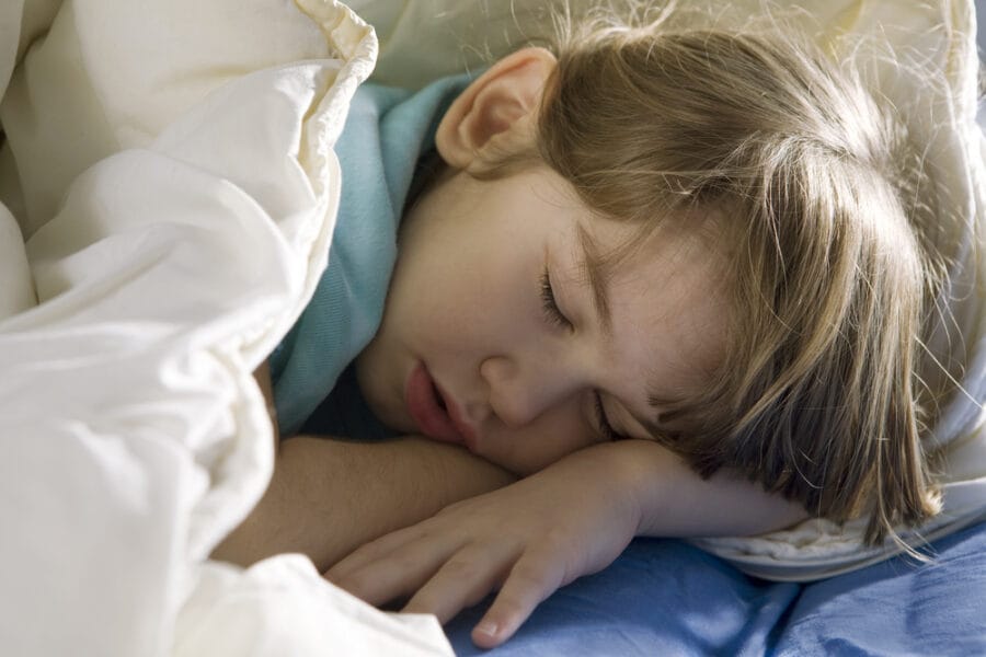 Young child asleep on a bed under blankets, representing topics related to nighttime routines and managing a child’s bed-wetting with comfort and care