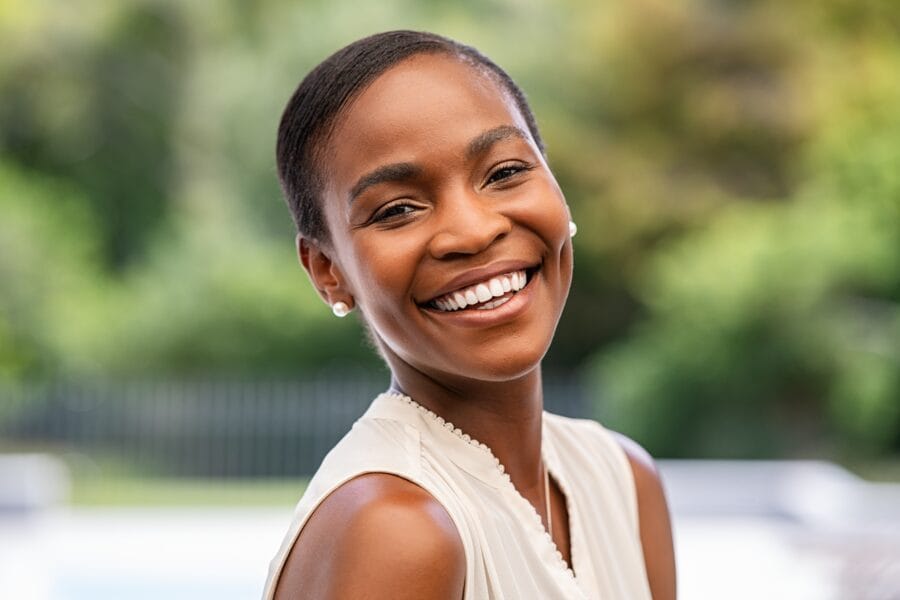Confident woman with a bright, joyful smile against a blurred outdoor background, symbolizing timeless beauty and lasting confidence, just like the charm of St. Augustine