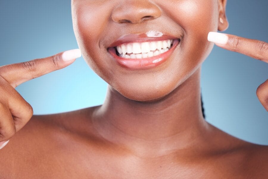 Close-up of a woman pointing to her radiant, healthy smile with white teeth against a blue background, representing confidence, beauty, and the power of your smile